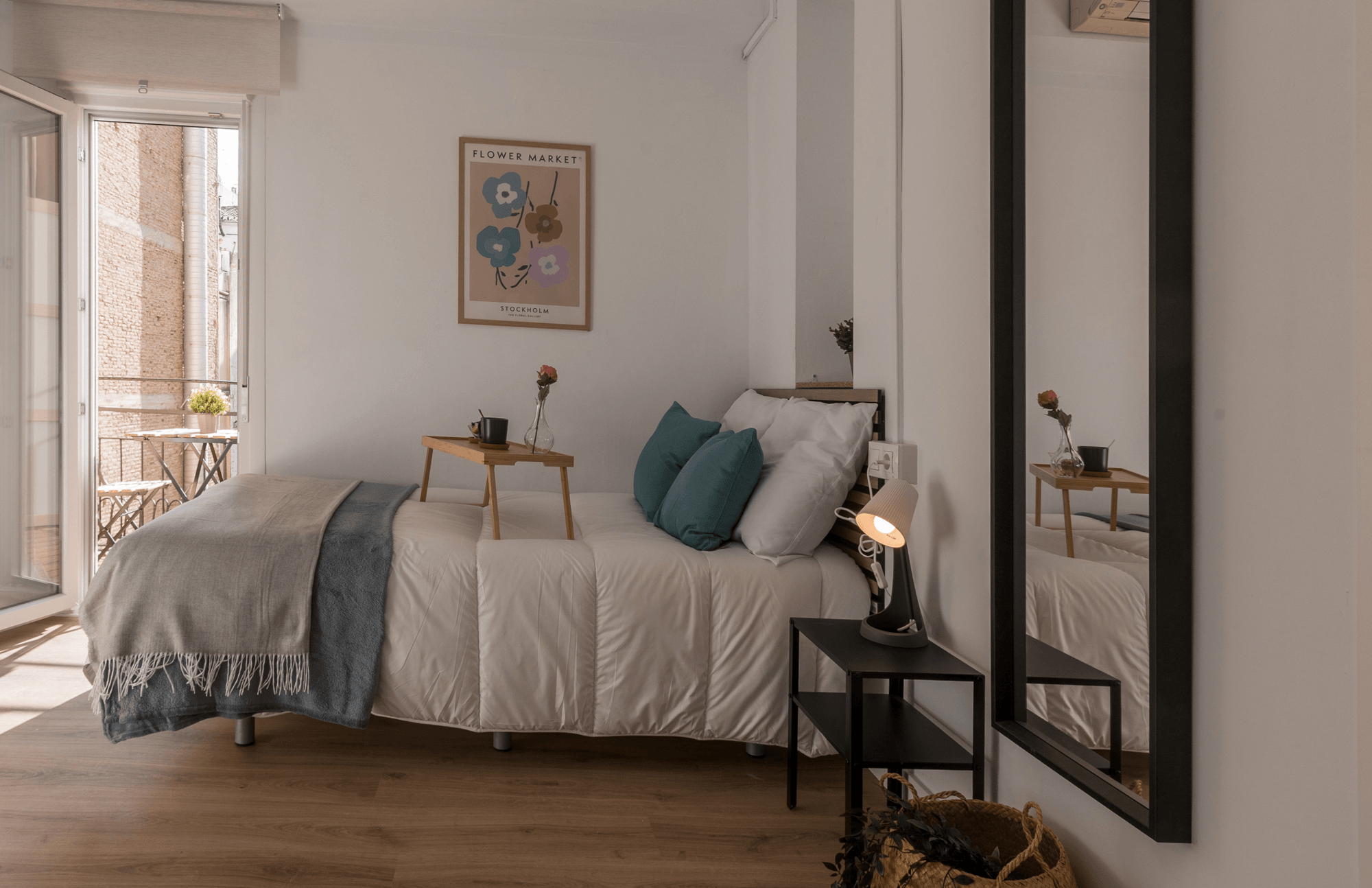 Fotografía de un dormitorio reformado por Vallecasas, con cama, mesilla, espejo y una ventana que da a un balconcito